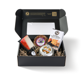 Schwarze Display-Schachtel mit 2 verschiedenen Käsesorten, Feigenbrot, Crackern und einem Glas Honig präsentiert.