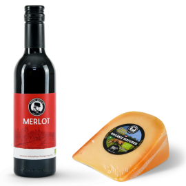 A small bottle of red wine paired with a piece of cheese.