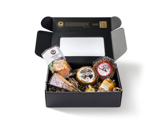 Sechs verschiedene Produkte in einer schwarzen Sichtfenster-Box, darunter Baby-Käse, Käse-Dip und Käsewaffeln.