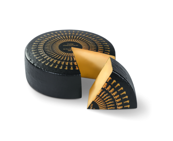 Bio Pure Perfection cheese wheel with a piece cut out. The piece is in front of the wheel.