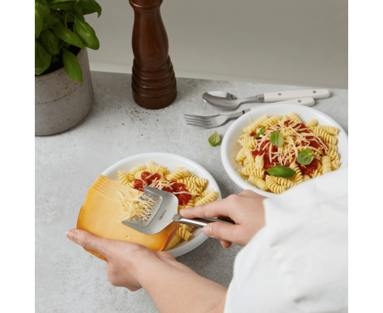 Two plates of pasta with cheese being grated over them.