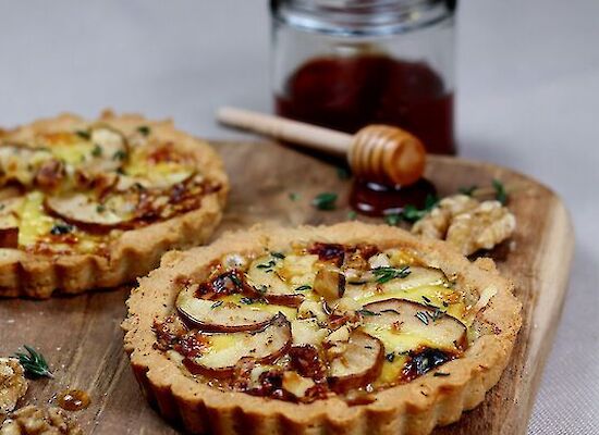 Tartlet with fenugreek cheese on a wooden board with a honey jar and dipper.