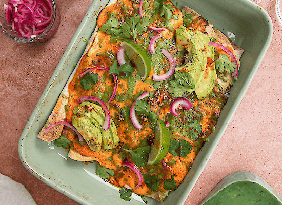 Plat au four avec des enchiladas au poulet, avocat, oignon rouge mariné et fromage de vache jalapeño fondu, garni de coriandre et de citron vert