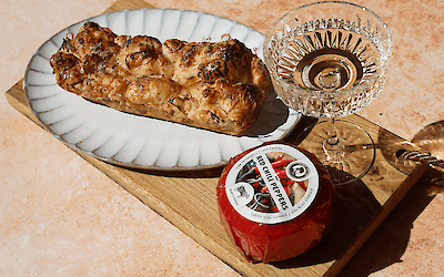 Pain à partager swavory au croissant avec fromage au chili Henri Willig fondant et hot honey, servi sur une planche en bois avec un verre de vin.