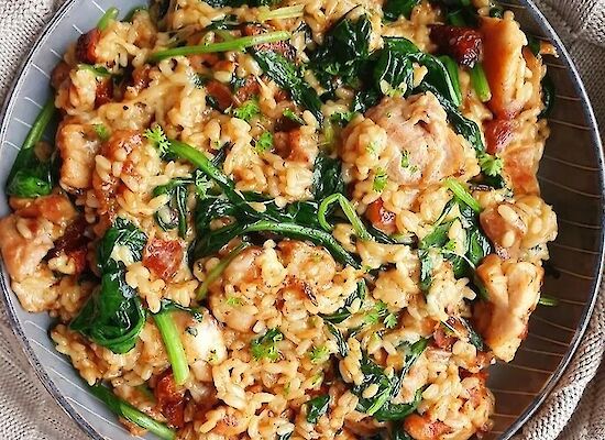 Creamy risotto with spinach, chunks of chorizo and melted cheese served on a dark plate, garnished with fresh parsley.